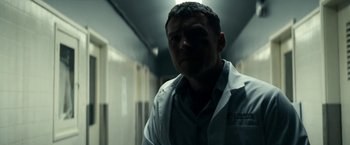 Movie still from “Fractured” (2019), directed by Brad Anderson – A man standing in a hallway with a light shining on him; Close Up shot, Low angle