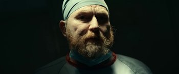 Movie still from “Fractured” (2019), directed by Brad Anderson – A man with a long beard and a bandage on his head; Close Up shot, Low angle
