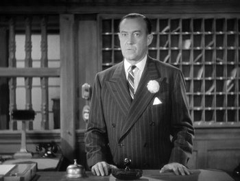 Movie still from “My Favorite Wife” (1940), directed by Garson Kanin – A man wearing a suit and tie standing in front of a counter; Medium shot, Low angle