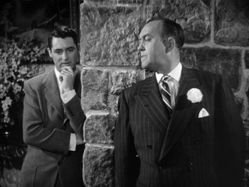 Movie still from “My Favorite Wife” (1940), directed by Garson Kanin – Two men in suits standing next to a stone wall; Medium shot, Over the shoulder angle
