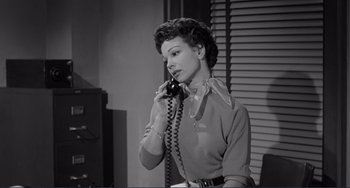 Movie still from “My Gun Is Quick” (1957), directed by Victor Saville – A woman is talking on a phone while sitting at a desk; Medium shot, Low angle
