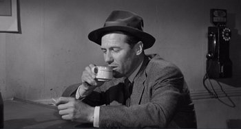 Movie still from “My Gun Is Quick” (1957), directed by Victor Saville – A black and white photo of a man drinking a cup of coffee; Close Up shot, High angle