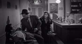 Movie still from “My Gun Is Quick” (1957), directed by Victor Saville – A man and a woman are standing in front of a counter; Medium shot, High angle