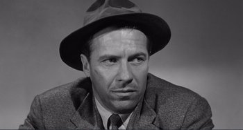 Movie still from “My Gun Is Quick” (1957), directed by Victor Saville – A man wearing a suit and a hat; Close Up shot, Low angle