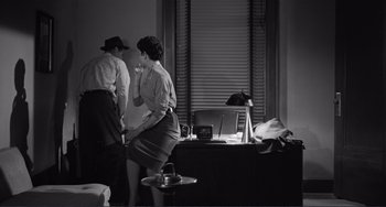 Movie still from “My Gun Is Quick” (1957), directed by Victor Saville – A man and a woman standing in front of a desk; Medium shot, High angle