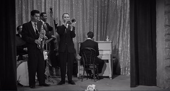 Movie still from “My Gun Is Quick” (1957), directed by Victor Saville – A black and white photo of a man playing the trumpet; Wide shot, High angle