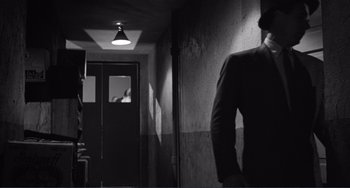 Movie still from “My Gun Is Quick” (1957), directed by Victor Saville – A man standing in a hallway with a light on; Wide shot, Low angle