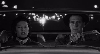 Movie still from “My Gun Is Quick” (1957), directed by Victor Saville – A black and white photo of a man and a woman in the back of a car; Medium shot, Low angle