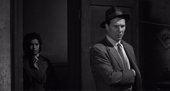 Movie still from “My Gun Is Quick” (1957), directed by Victor Saville – A black and white photo of a man in a suit and hat; Medium shot, Low angle