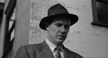Movie still from “My Gun Is Quick” (1957), directed by Victor Saville – Black and white photograph of a man wearing a suit and a hat; Close Up shot, Low angle