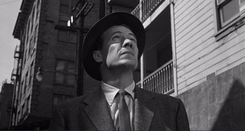 Movie still from “My Gun Is Quick” (1957), directed by Victor Saville – A black and white photo of a man in a suit and hat; Close Up shot, Low angle
