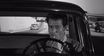 Movie still from “My Gun Is Quick” (1957), directed by Victor Saville – A black and white photo of a man driving a car; Close Up shot, High angle