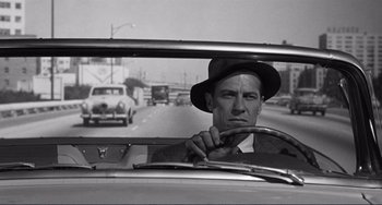 Movie still from “My Gun Is Quick” (1957), directed by Victor Saville – A black and white photo of a man driving a car; Medium shot, Over the shoulder angle