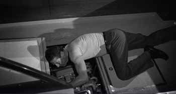 Movie still from “My Gun Is Quick” (1957), directed by Victor Saville – A man laying on the ground working on a machine; Medium shot, High angle