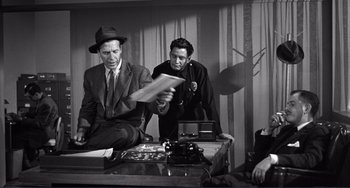 Movie still from “My Gun Is Quick” (1957), directed by Victor Saville – Two men sitting at a table and one is reading a newspaper; Medium shot, Over the shoulder angle