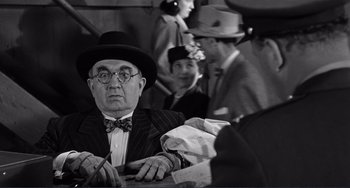 Movie still from “My Gun Is Quick” (1957), directed by Victor Saville – An older man in a suit and hat sitting at a table with other people; Close Up shot, Over the shoulder angle