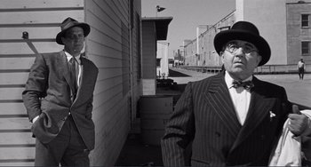 Movie still from “My Gun Is Quick” (1957), directed by Victor Saville – A man in a suit and hat standing next to another man in a suit and hat; Medium shot, Low angle