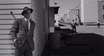 Movie still from “My Gun Is Quick” (1957), directed by Victor Saville – A black and white photo of a man in a suit and hat; Wide shot, Low angle