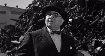 Movie still from “My Gun Is Quick” (1957), directed by Victor Saville – An older man wearing a suit and a bow tie in front of a pile of bicycles; Close Up shot, Low angle