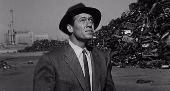 Movie still from “My Gun Is Quick” (1957), directed by Victor Saville – A black and white photo of a man wearing a suit and a hat; Medium shot, Low angle