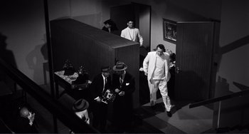 Movie still from “My Gun Is Quick” (1957), directed by Victor Saville – A black and white photo of a group of men in suits and hats; Wide shot, High angle