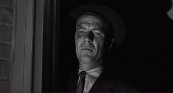 Movie still from “My Gun Is Quick” (1957), directed by Victor Saville – Black and white photograph of a man in a suit and hat; Close Up shot, Low angle