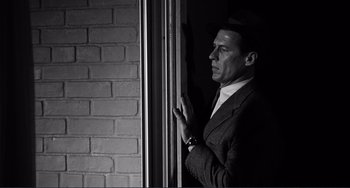 Movie still from “My Gun Is Quick” (1957), directed by Victor Saville – A black and white photo of a man in a suit looking out of a window; Medium shot, Low angle