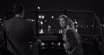 Movie still from “My Gun Is Quick” (1957), directed by Victor Saville – An old photo of a man and a woman standing in front of a window; Medium shot, Over the shoulder angle