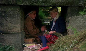 Movie still from “My Life as a Dog” (1985), directed by Lasse Hallström – Two children sitting in a cave with a book; Wide shot, High angle