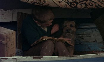 Movie still from “My Life as a Dog” (1985), directed by Lasse Hallström – A boy reading a book to a dog under a blanket; Medium shot, High angle