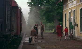 Movie still from “My Life as a Dog” (1985), directed by Lasse Hallström – A group of people standing on the side of a train track; Wide shot, Over the shoulder angle
