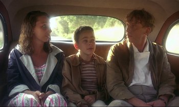 Movie still from “My Life as a Dog” (1985), directed by Lasse Hallström – Three people sitting in the back of a car; Medium shot, Over the shoulder angle