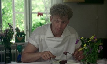 Movie still from “My Life as a Dog” (1985), directed by Lasse Hallström – A man sitting at a table with a plate of food in front of him; Close Up shot, Over the shoulder angle