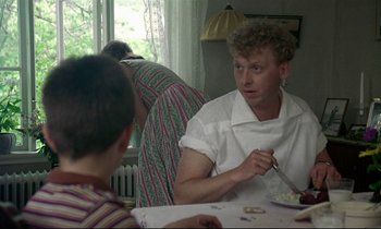 Movie still from “My Life as a Dog” (1985), directed by Lasse Hallström – A man sitting at a table with a knife in his hand; Medium shot, Over the shoulder angle