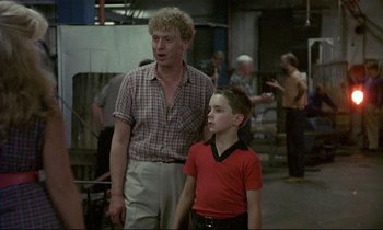 Movie still from “My Life as a Dog” (1985), directed by Lasse Hallström – A man standing next to a young girl in a red shirt; Medium shot, Over the shoulder angle