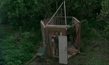 Movie still from “My Life as a Dog” (1985), directed by Lasse Hallström – A man standing in front of an outhouse in the woods; Wide shot, High angle
