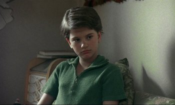 Movie still from “My Life as a Dog” (1985), directed by Lasse Hallström – A boy in a green shirt is sitting on a couch; Close Up shot, High angle