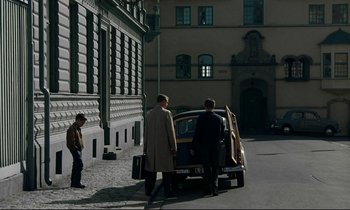 Movie still from “My Life as a Dog” (1985), directed by Lasse Hallström – Two men standing in front of a car; Wide shot, High angle