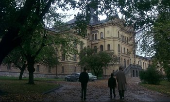 Movie still from “My Life as a Dog” (1985), directed by Lasse Hallström – Three people are standing in front of a large building; Extreme Wide shot, High angle