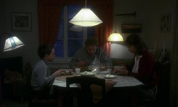 Movie still from “My Life as a Dog” (1985), directed by Lasse Hallström – Three people are sitting at a table with food; Wide shot, High angle
