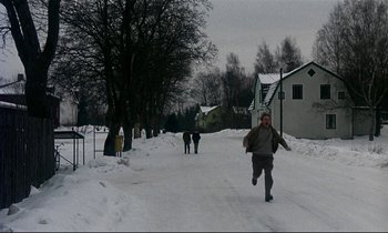 Movie still from “My Life as a Dog” (1985), directed by Lasse Hallström – A man running in the snow near a group of people; Wide shot, High angle