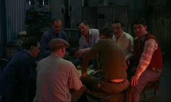 Movie still from “My Life as a Dog” (1985), directed by Lasse Hallström – A group of men sitting around each other in the dark; Wide shot, High angle