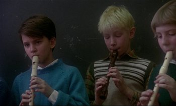 Movie still from “My Life as a Dog” (1985), directed by Lasse Hallström – Two young boys are sitting and playing a musical instrument; Medium shot, Low angle