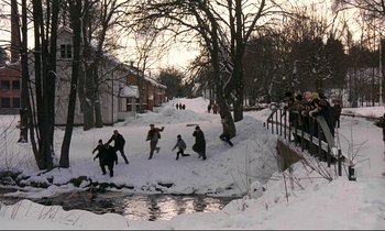 Movie still from “My Life as a Dog” (1985), directed by Lasse Hallström – A group of people are playing in the snow near a stream; Extreme Wide shot, High angle
