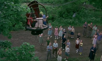 Movie still from “My Life as a Dog” (1985), directed by Lasse Hallström – A group of people standing in a forest next to a cable car; Wide shot, Overhead angle