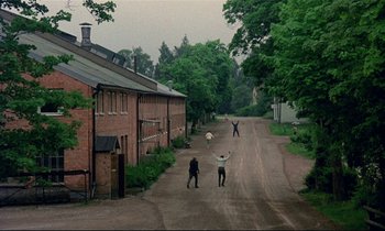 Movie still from “My Life as a Dog” (1985), directed by Lasse Hallström – A group of people standing on a dirt road near a building; Extreme Wide shot, High angle