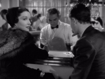 Movie still from “My Man Godfrey” (1936), directed by Gregory La Cava – A man and a woman sitting at a table with a man smoking a cigarette; Medium shot, Over the shoulder angle