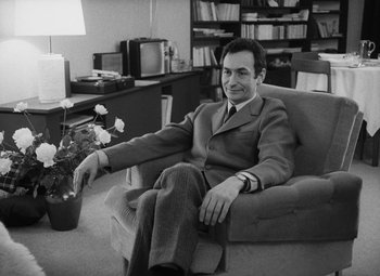 Movie still from “My Night at Maud's” (1969), directed by Éric Rohmer – Black and white photograph of a man sitting on a couch; Medium shot, Low angle