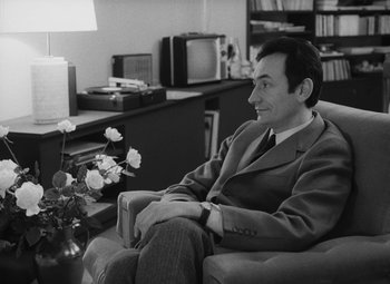 Movie still from “My Night at Maud's” (1969), directed by Éric Rohmer – A black and white photo of a man sitting in a chair; Medium shot, Over the shoulder angle