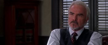 Movie still from “Mystery, Alaska” (1999), directed by Jay Roach – A man sitting in a chair wearing a vest; Close Up shot, Over the shoulder angle